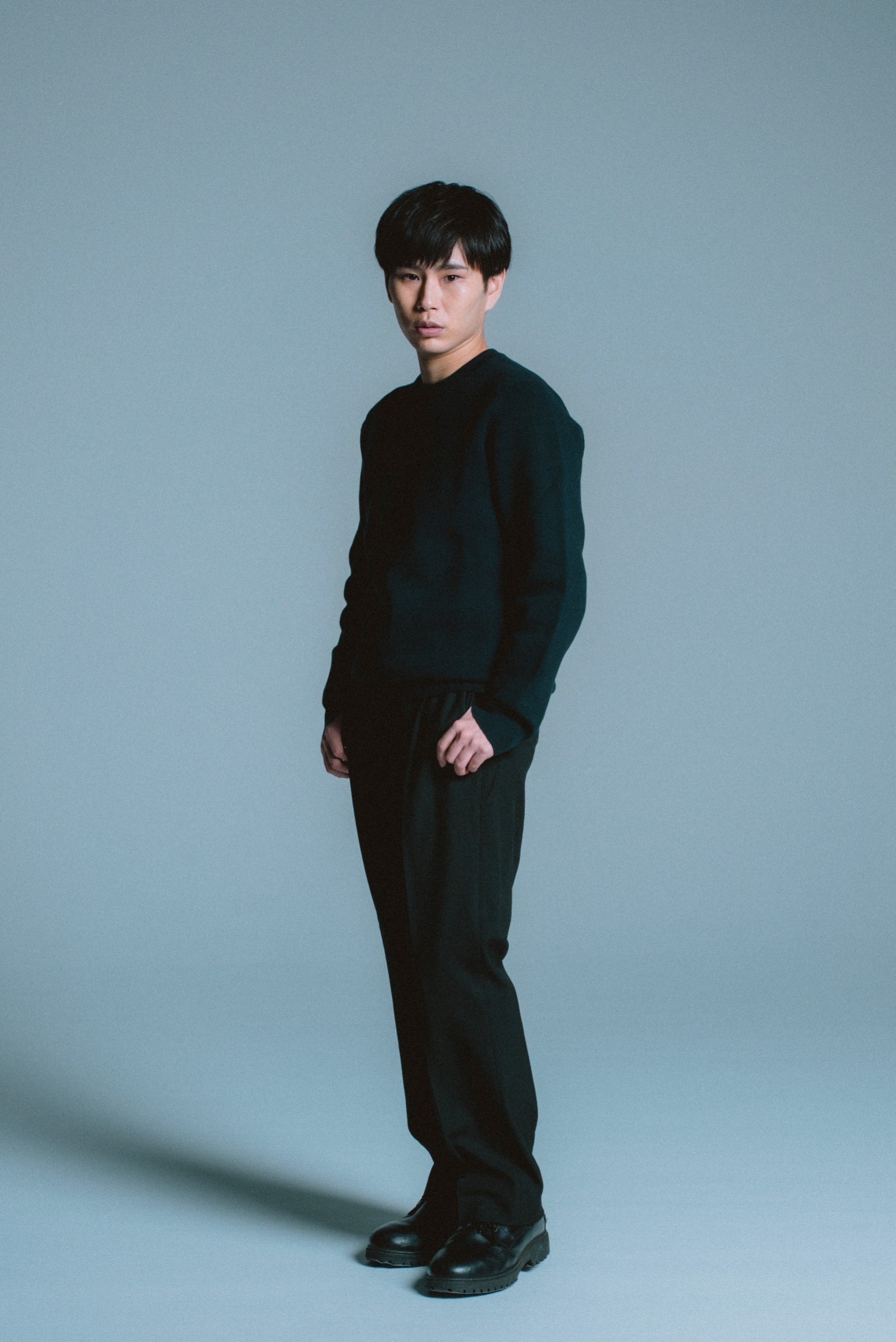 黒い衣装で立つ政野郁弥の全身ポートレート