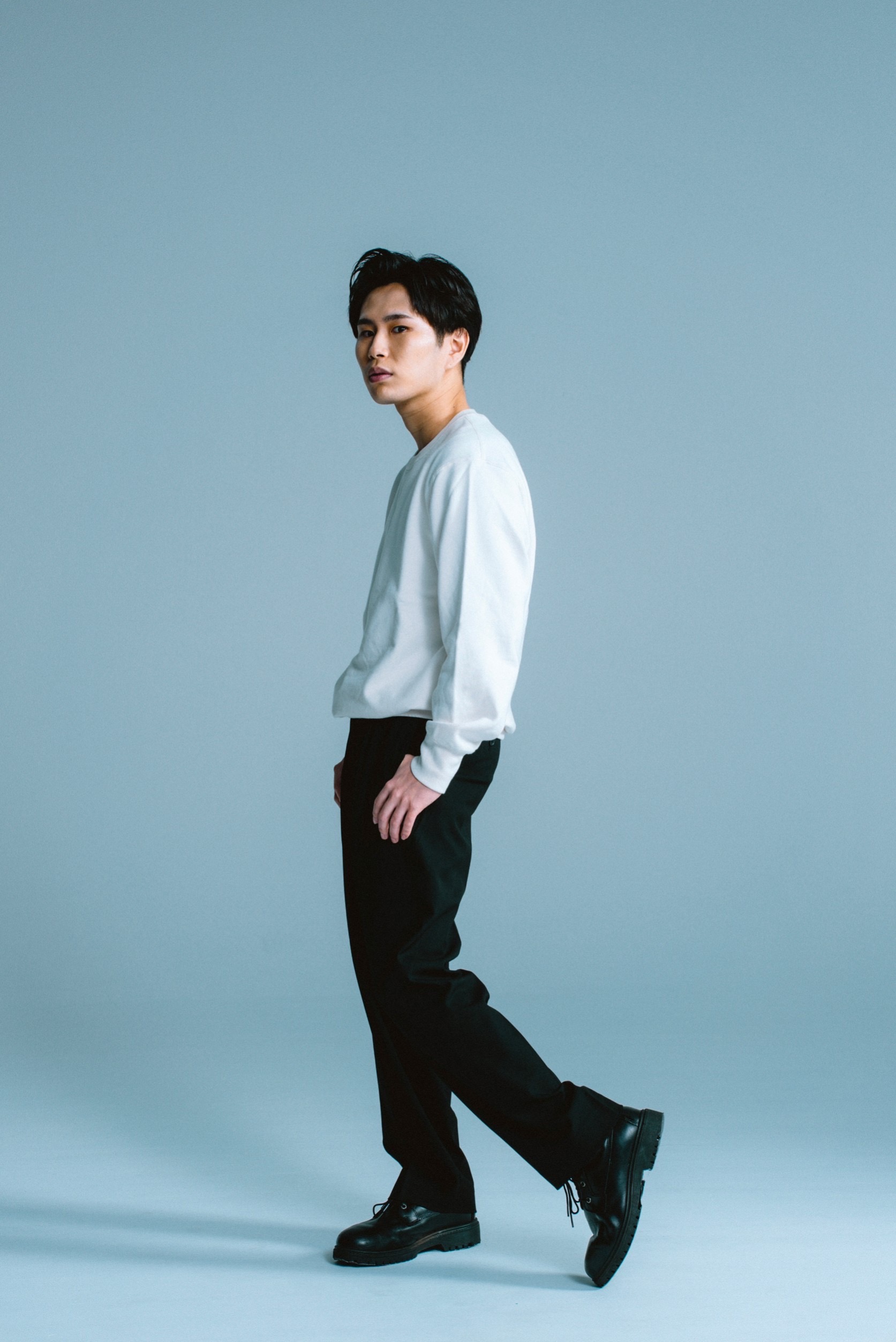 白いシャツと黒いパンツを着た政野郁弥の全身写真